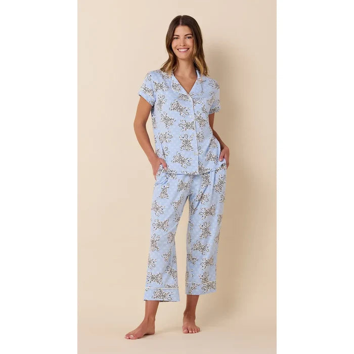 A woman modeling a light blue short-sleeve pajama set with a delicate floral print, standing against a solid beige background.