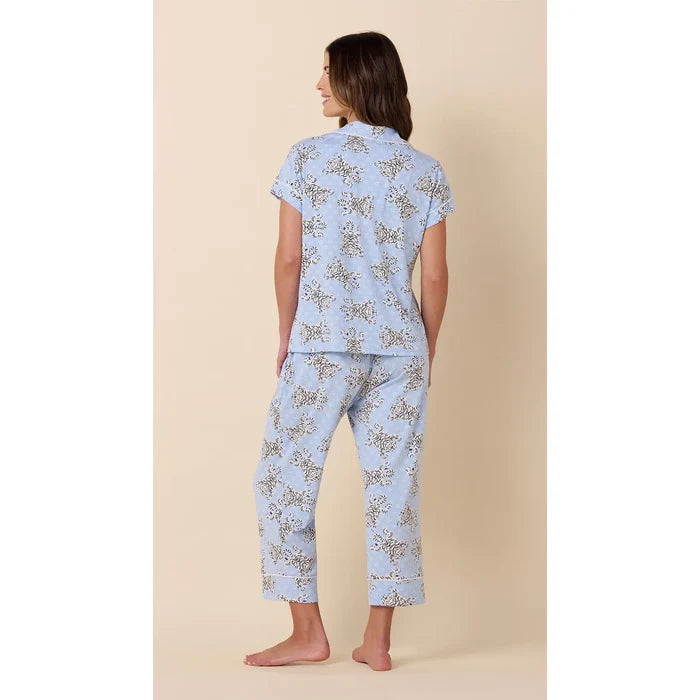 A woman shown from the back wearing a light blue pajama set with a delicate beige and brown floral pattern, standing against a solid beige background.