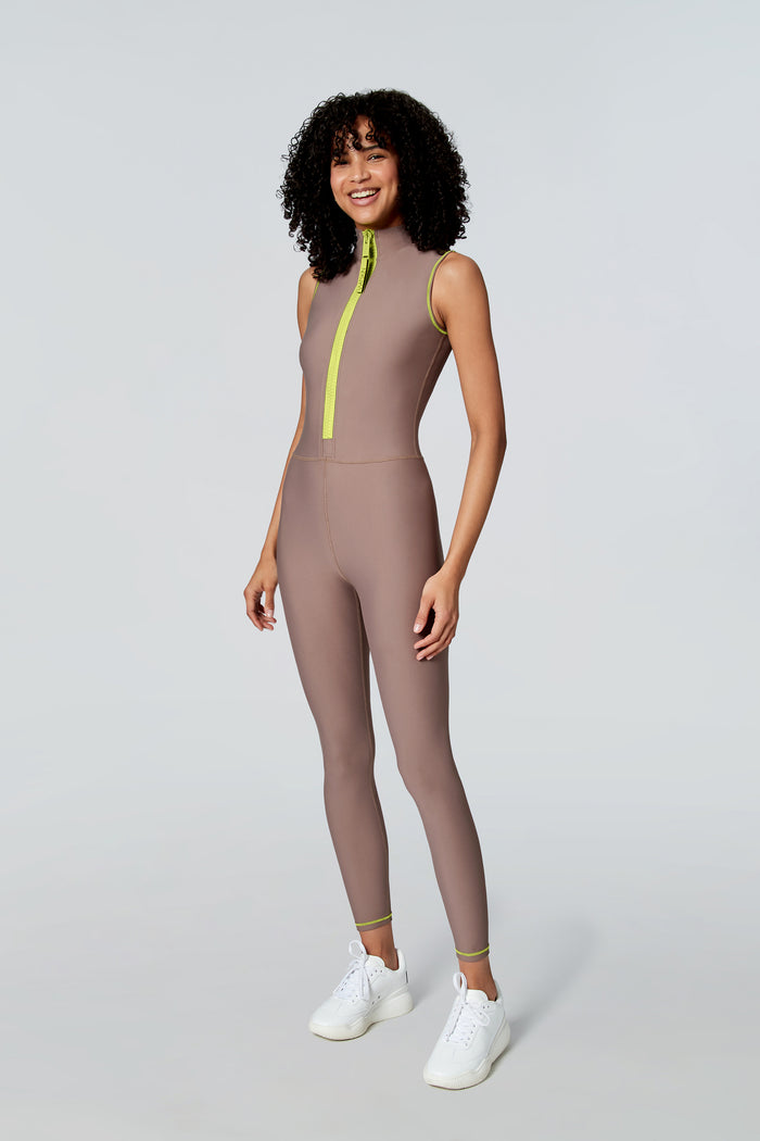 Female model wearing Watskin Chloe sleeveless catsuit in Taupe featuring a neon front zipper
