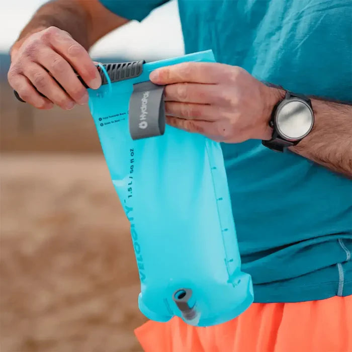 Man opening the HydraPak Velocity Hydration Water Reservoir, demonstrating its wide top opening for easy filling and cleaning during outdoor use.  from  John Bull Clothing