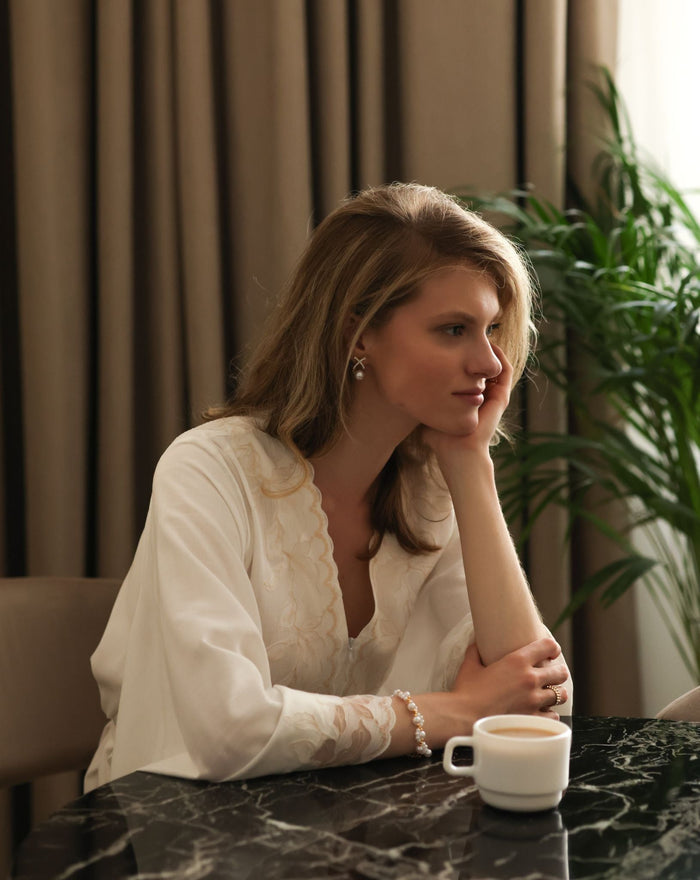 A woman sitting by a table in a soft cotton robe, capturing a moment of quiet sophistication and daily comfort.