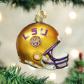 A gold and purple LSU football helmet ornament with a tiger logo hangs on a Christmas tree, surrounded by green branches and soft, out-of-focus lights in the background.