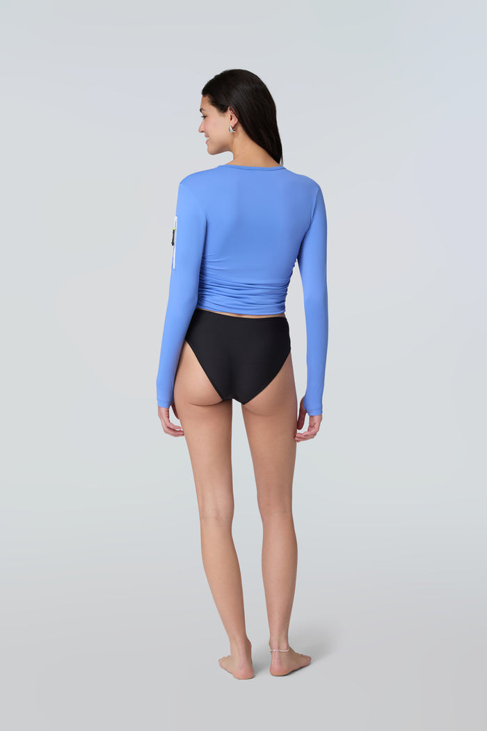 Back view of a woman wearing a light blue long-sleeve sun protective tee and black bikini bottom