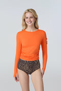 Front view of a woman wearing an orange long-sleeve sun protective tee with side ruching and arm zip pocket and leopard print bikini bottom