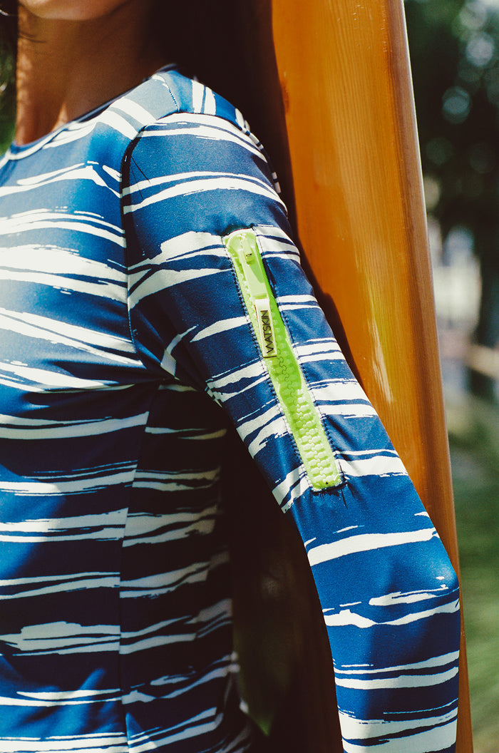 Close-up of a person wearing a blue and white striped shirt with a yellow zipper pocket on the arm in a tropical outdoor setting