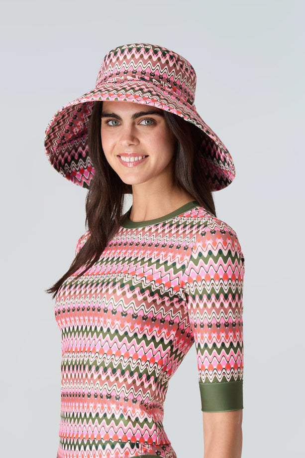 Woman wearing a pink and green wavy striped patterned wide brimmed sun hat, short sleeve swim top with green sleeve cuff