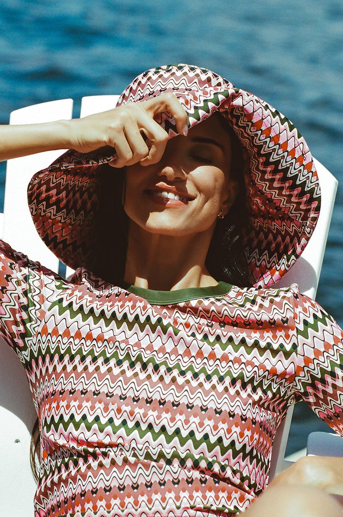 Pink & green wavy stripe sun hat, swim top with green cuffs, bikini bottom, dock by water