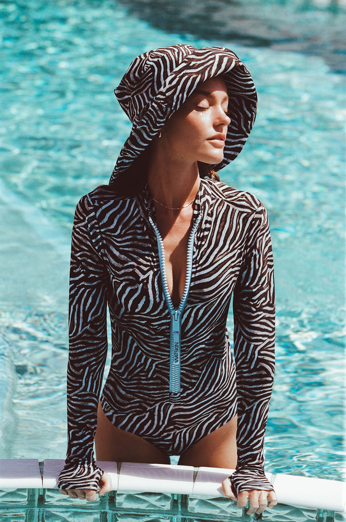 Woman standing in swimming pool wearing Watskin bodysuit and Sienna sunhat in Blue Zebra