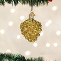 A gold, glittery pine cone ornament hangs from a Christmas tree branch with blurred white holiday lights glowing softly in the background.