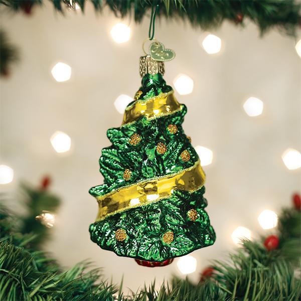 A shiny green glass Christmas tree ornament with gold ribbon and glitter accents hangs from a tree branch, with blurred white lights in the background.
