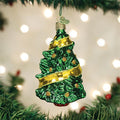 A shiny green glass Christmas tree ornament with gold ribbon and glitter accents hangs from a tree branch, with blurred white lights in the background.